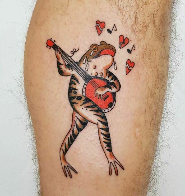 American traditional tattoo of a frog playing a banjo, surrounded by music notes and hearts.