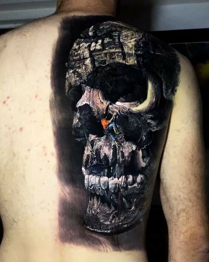 Realistic tattoo art of a skull with climber, showcasing detailed design on a person's back.