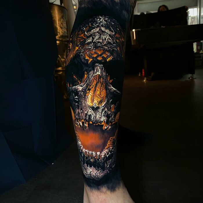 Intricate skull tattoo art with fiery orange and black details on leg, demonstrating artistic tattoo mastery.