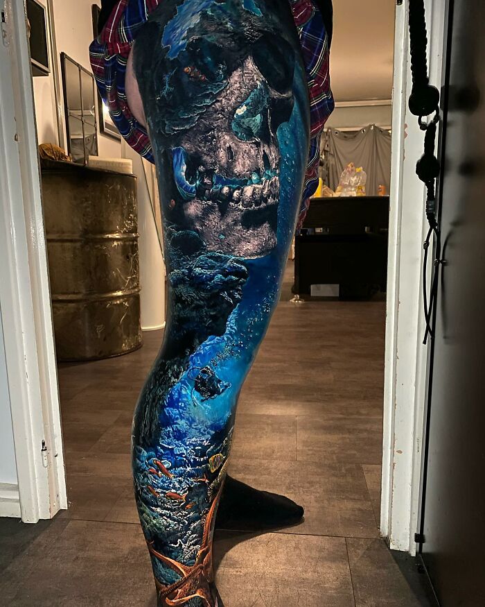 Tattoo art depicting a detailed underwater scene with a skull on a person's leg.