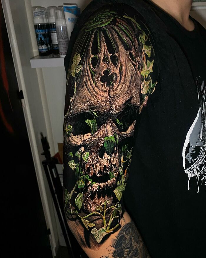 Arm tattoo art depicting a skull intertwined with ivy leaves, showcasing intricate detail.