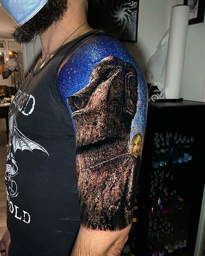 Tattoo art featuring a detailed Moai statue on an arm, with a starry sky background, showcasing advanced design techniques.