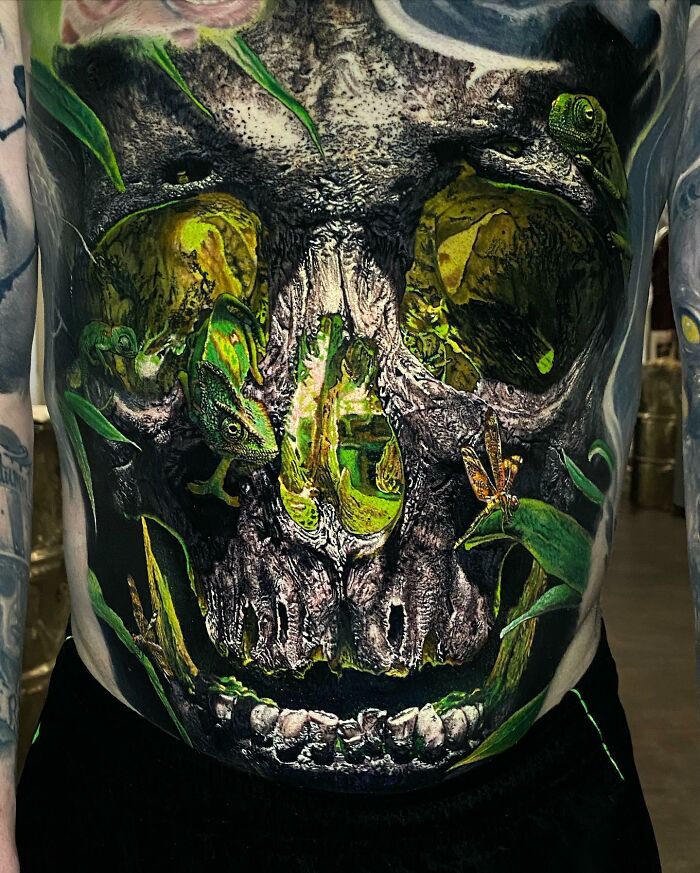 Detailed tattoo art of a skull with vibrant green elements and animals, showcasing artistic mastery in tattoo design.