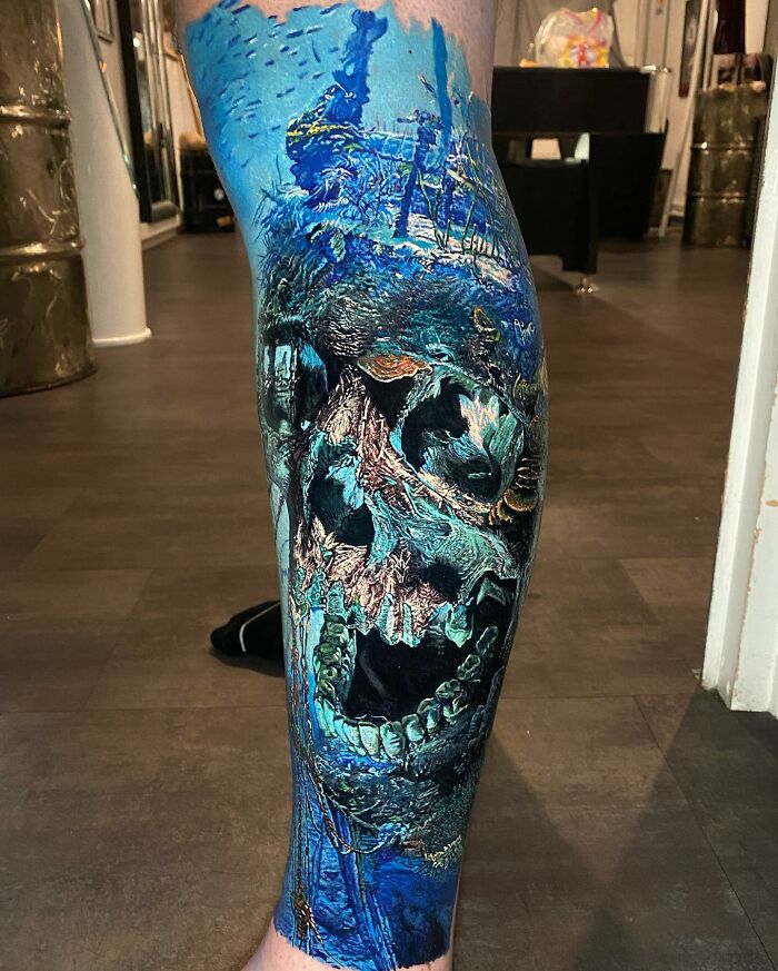 Vivid tattoo art depicting a blue underwater scene with a skull design on a person's leg.