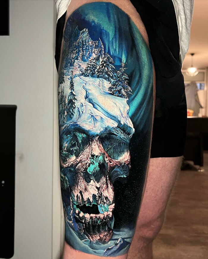 Tattoo art depicting a skull with an ice and snow landscape design on the thigh.