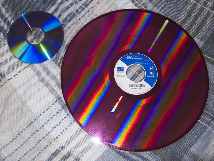 Two old gadgets, a compact disc and a larger vintage laserdisc, displaying colorful reflections on fabric.