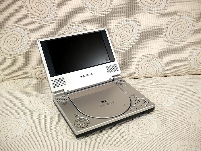 Portable DVD player from the collection of old gadgets that were the trendsetters of their time displayed on fabric surface.