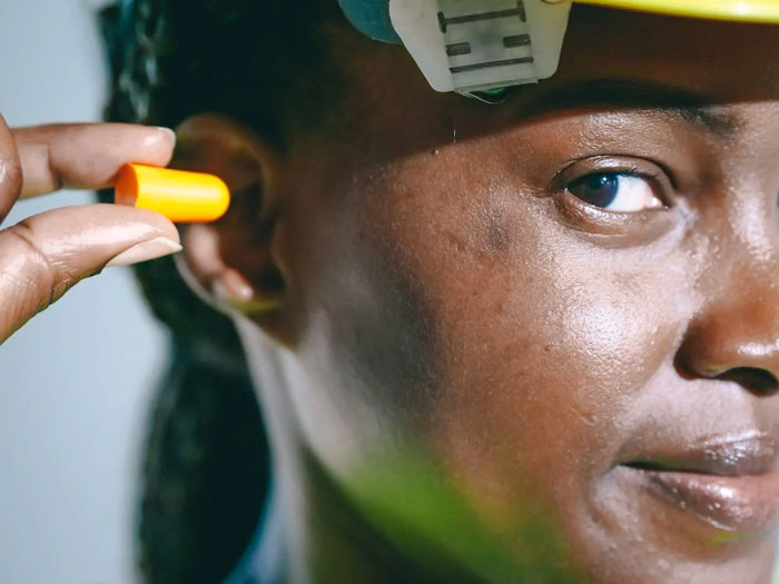 Close-up of a person over the age of 50 inserting an earplug, symbolizing advice shared for younger people.