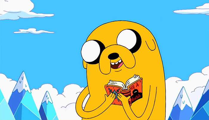 Jake the Dog from Adventure Time holding a book against a snowy mountain backdrop with blue skies and clouds.