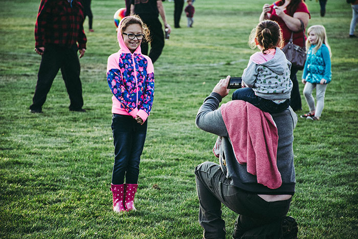 Man Carrying Toddler on His Neck Taking Photo of Standing Girl in Front of Him