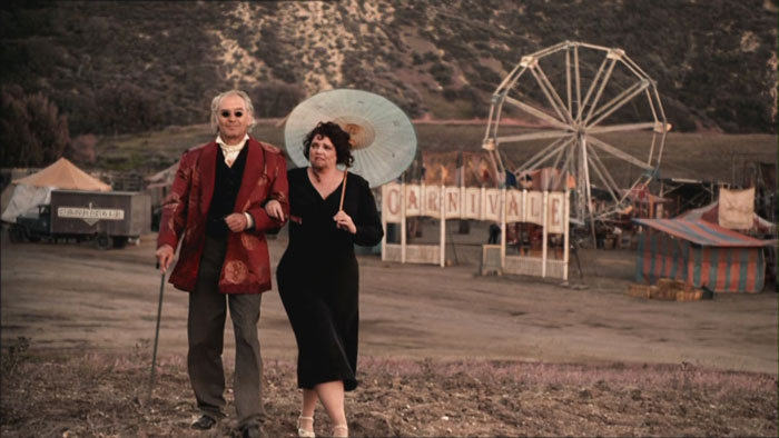 Man with a walking stick and a woman with an umbrella walking 