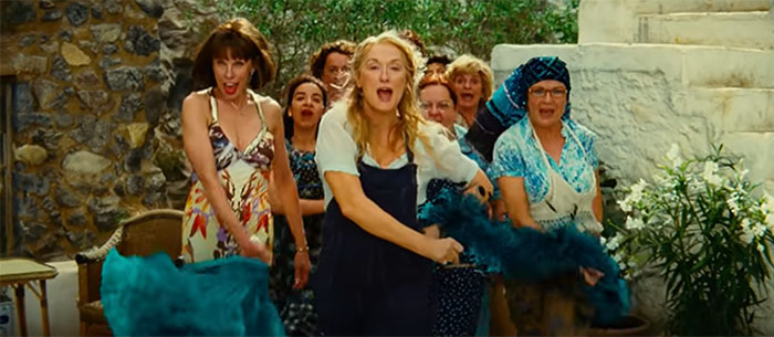 Scene from Mamma Mia! featuring joyful women dancing outdoors, celebrating love in one of the best wedding movies ever made