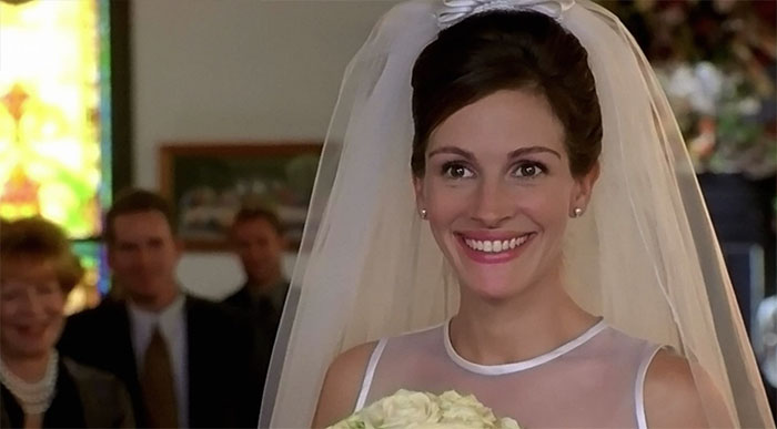 Julia Roberts smiling in a wedding dress holding a bouquet, a scene from the best wedding movies celebrating love.