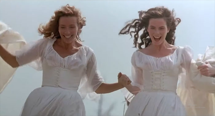 Two women in white dresses joyfully running and holding hands in a scene from a classic wedding movie celebrating love.