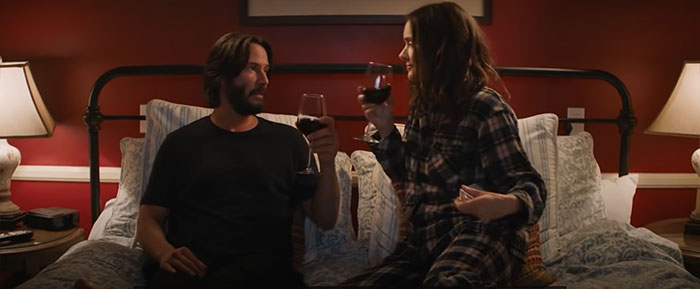 Scene from Palm Springs movie showing a couple toasting wine in bed, highlighting popular wedding movies.