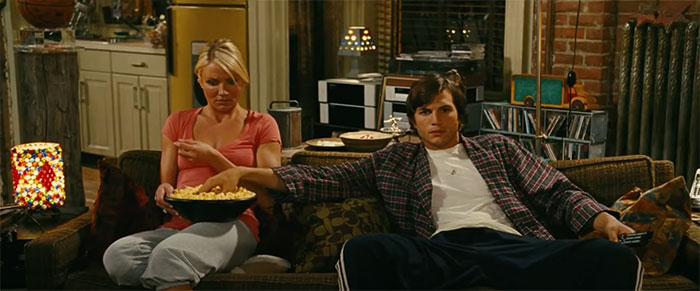 Scene from wedding movie What Happens In Vegas showing a couple sitting on a couch sharing popcorn in a cozy living room.