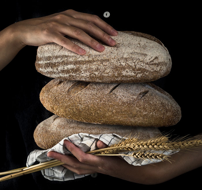 Person carrying thee loafs of bread 