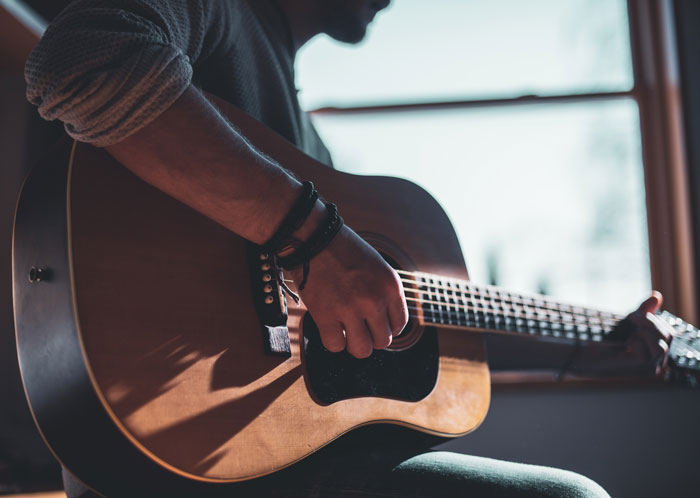 Man playing a guitar near a window 
