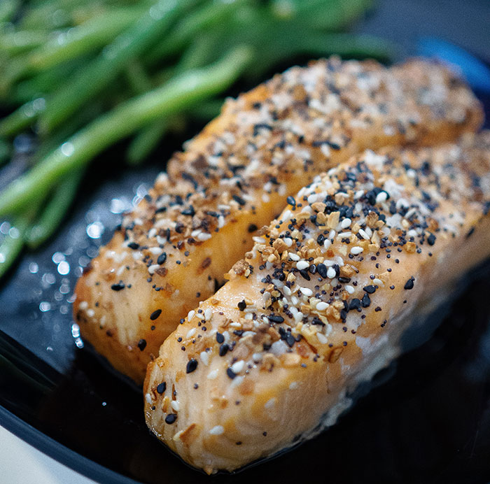 Fried and seasoned salmon with green leafy vegetable on black ceramic plate
