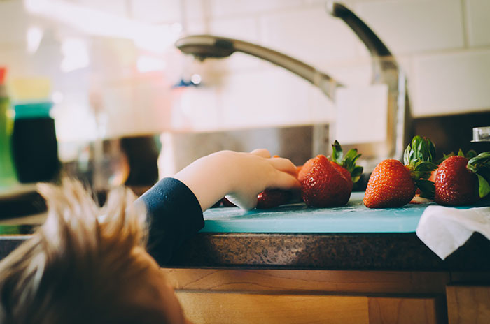 Child picking strawberries in kitchen