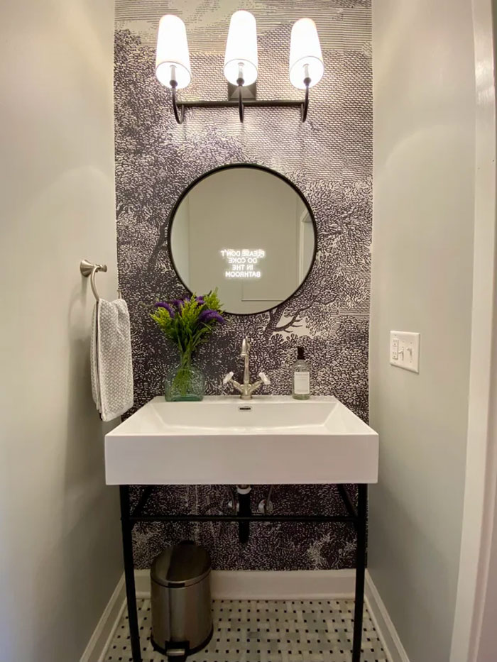 Bathroom decoration idea with round mirror, patterned wall, and elegant lighting above modern sink.