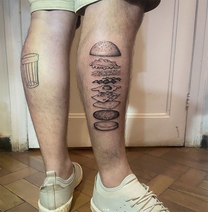 Burger tattoo design on a person's leg, featuring detailed layers, showcasing delicious food tattoos.
