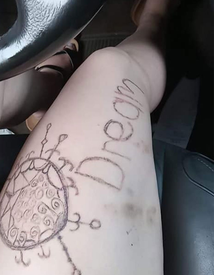 Leg with an amateur tattoo fail showing a misspelled word and a poorly drawn design on pale skin in a car interior.