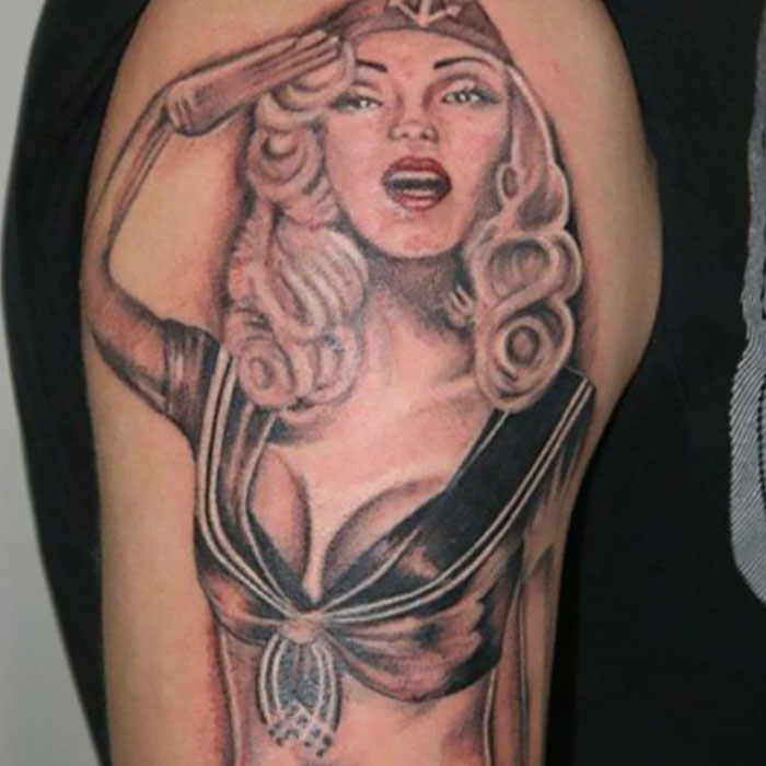 Tattoo fail of a woman in a sailor outfit with uneven features and distorted proportions on upper arm.
