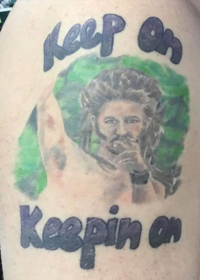 Tattoo fail of a poorly drawn person with the text keep on Keepin on in dark ink and a green background.