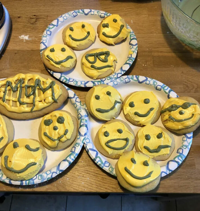 Unappetizing cookies with yellow icing, uneven smiley faces, and "MUM" message on paper plates.