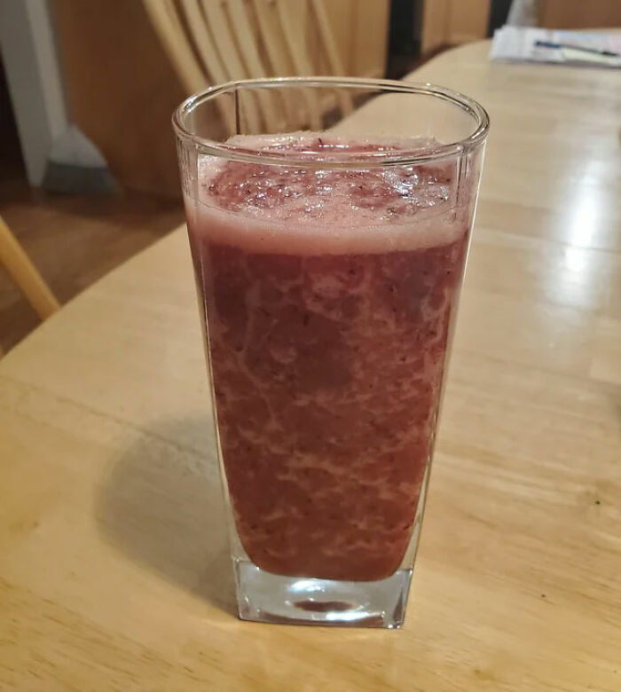 Unappetizing thick reddish beverage in a tall glass on a wooden table.