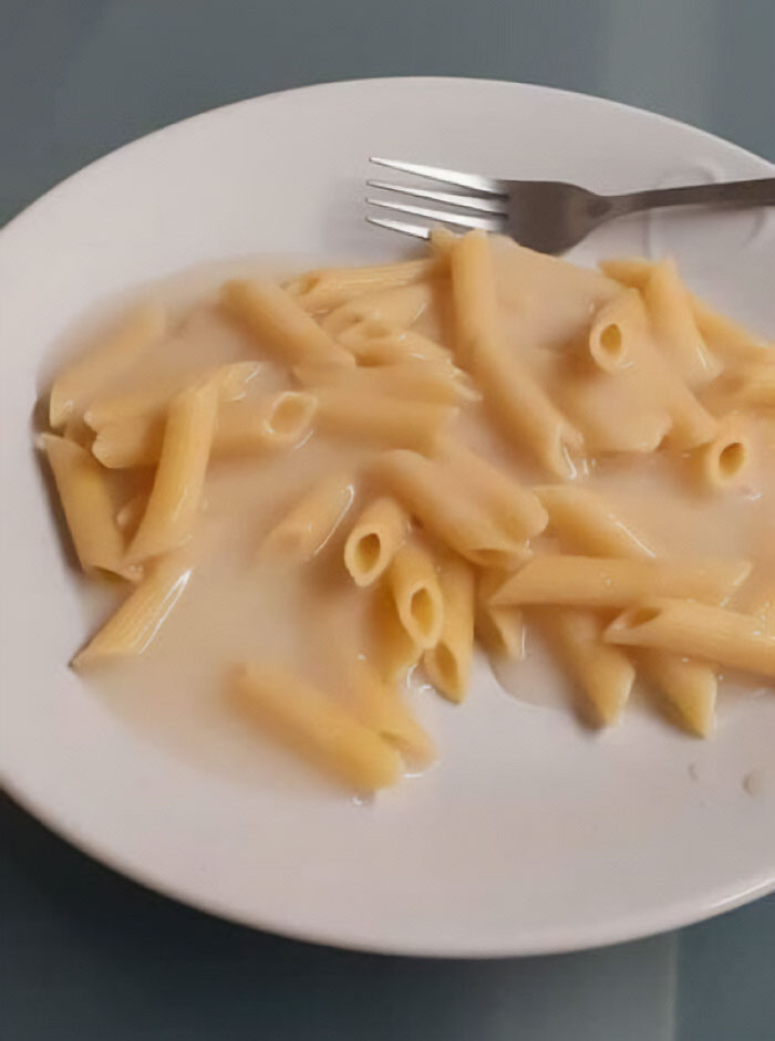 Unappetizing food: a plate of penne pasta in a watery sauce with a fork on the side.