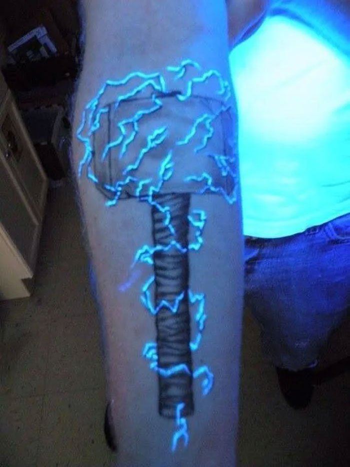 Marvel tattoo of Thor's hammer with glowing blue lightning on an arm.