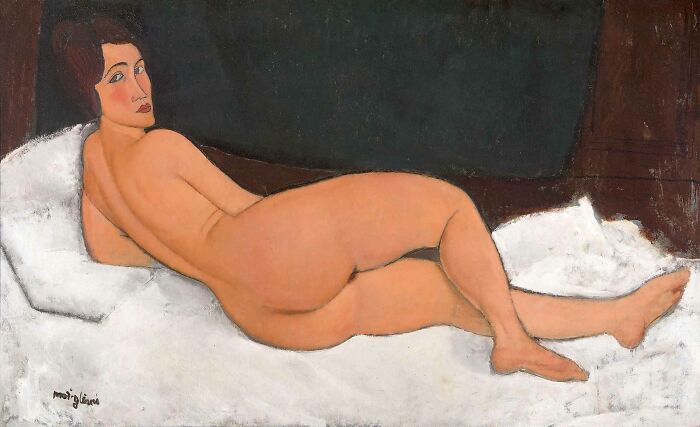 Reclining n**e (on the left side) by Amedeo Modigliani, 1917, oil painting features naked woman reclining on a couch