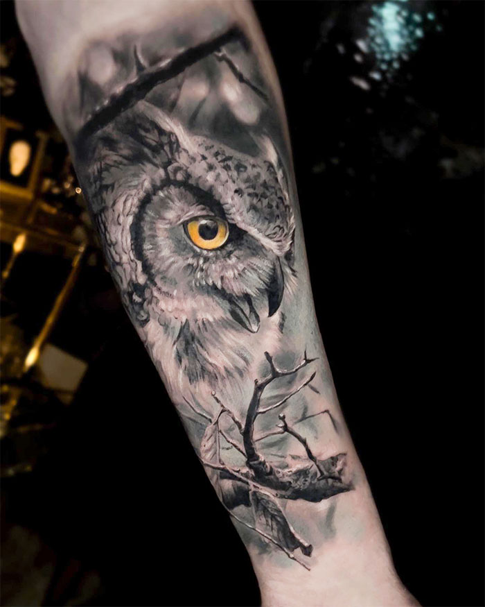 Detailed owl tattoo with nature elements on forearm, symbolizing the human-earth bond.