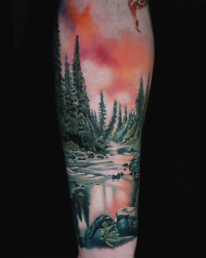 Nature tattoo featuring a forest landscape with a river and vibrant sky.