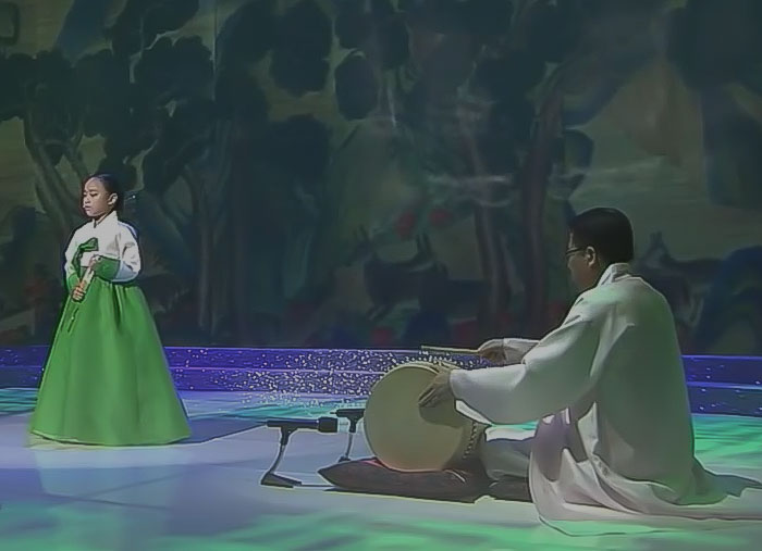 A girl singer in a green dress and a man drummer performing pansori on stage