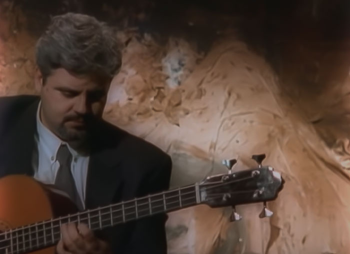 Image from Madredeus - Haja O Que Houver music video, a man in a suit playing guitar