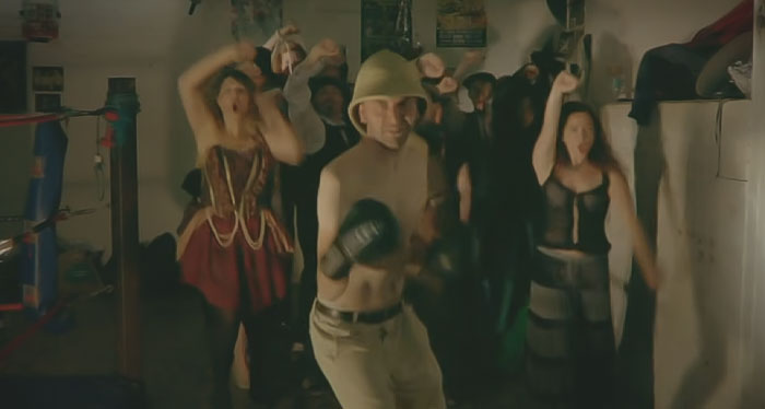 Scene from Fighting Trousers - Professor Elemental, a topless man boxing, and a group of people in the background