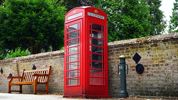 Red telephone booth near wooden bench and brick wall, showcasing classic old gadgets that were the trendsetters of their time.