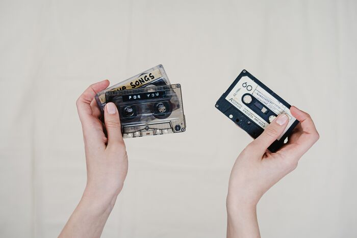 Person holding compact cassette tapes, showcasing old gadgets that were trendsetters in their time.