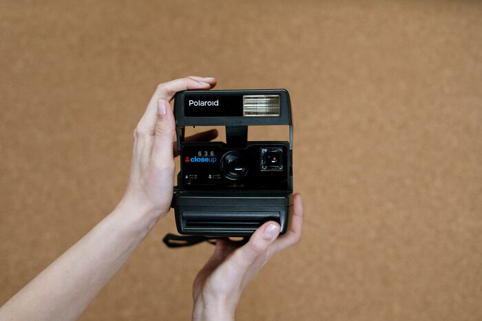 Person holding a vintage Polaroid camera, showcasing one of the old gadgets that were trendsetters of their time.