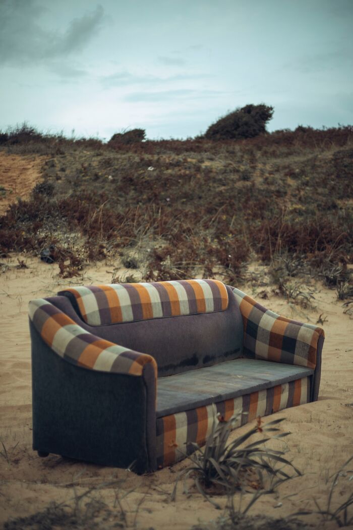 Striped couch on sandy beach under overcast sky; unique experience setting.
