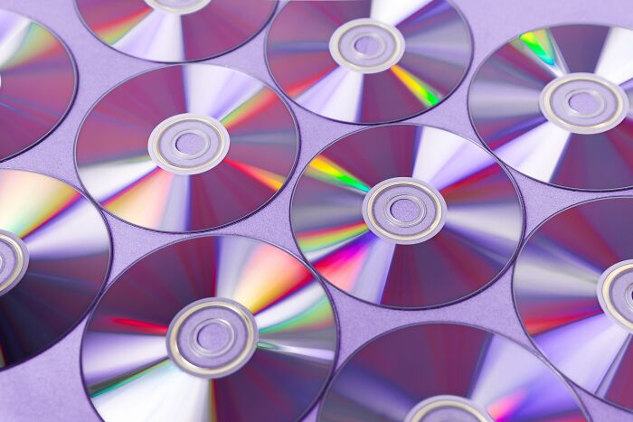Many old gadgets shown with a collection of DVD discs on a table reflecting colorful light patterns.
