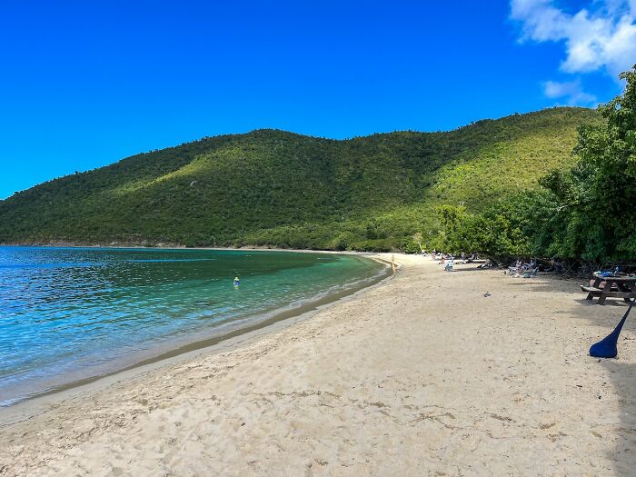 Sandy beach with clear water, lush green hills, and a bright blue sky, capturing a perfect vacation experience.