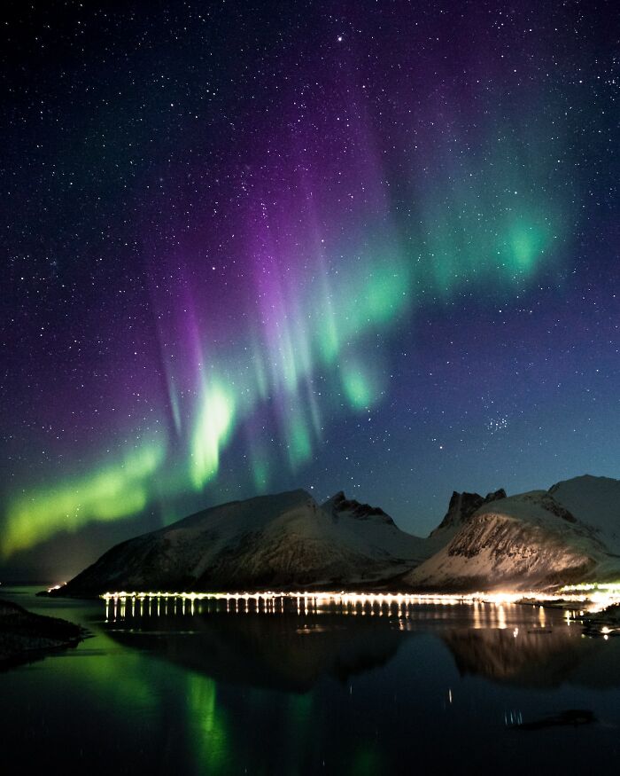 Northern lights over snowy mountains and reflective water, a breathtaking experience worth having at least once.