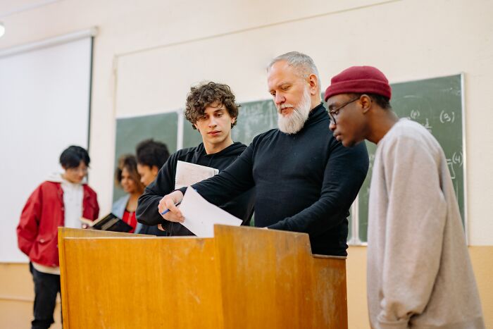 Lector Showing Papers To Couple Of Students 
