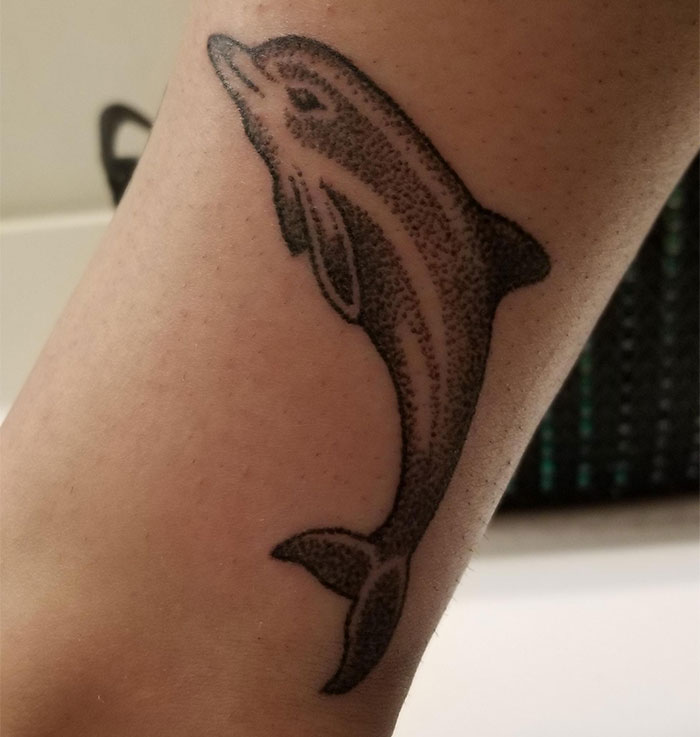 Tattoo design of a dolphin on skin, often considered lacking creativity.