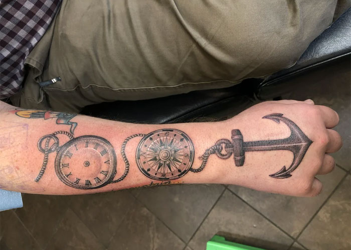 Forearm tattoo with a pocket watch, compass, and anchor, critiqued as lacking creativity.