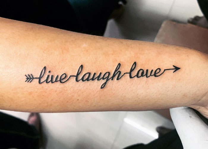 "Arm tattoo with 'live laugh love' phrase, a common tattoo design lacking creativity, according to online opinions."